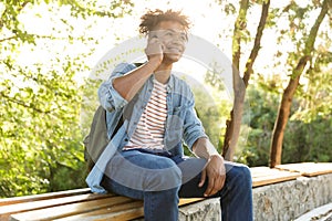 Emotional young african guy in park outdoors talking by mobile phone