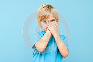 Emotional young boy covering face with hands isolated over pastel blue background. Mental wellbeing.