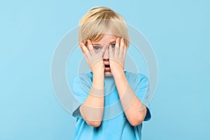 Emotional young boy covering face with hands isolated over pastel blue background. Mental wellbeing.