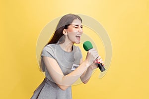 Emotional young girl, female reporter holding reporter microphone isolated on yellow studio background. Concept of