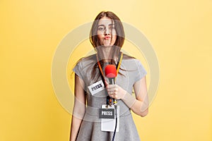 Emotional young girl, female reporter holding reporter microphone isolated on yellow studio background. Concept of