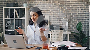 Emotional young lady skyping talking showing thumbs-up using laptop at work