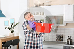 Emotional young man calling plumber while collecting water leakage from ceiling