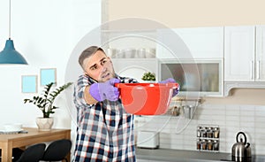 Emotional young man calling plumber while collecting water leakage from ceiling