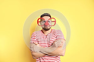 Emotional young man with glasses and clown nose on yellow background. April fool`s day