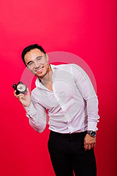 Emotional young man holding clock on red background. Being late concept