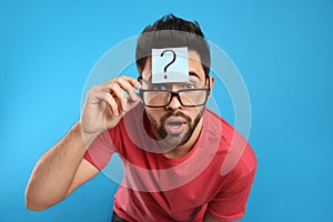 Emotional young man with question mark sticker on forehead against blue background