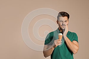 Emotional young man with sensitive teeth and ice cream on color background.