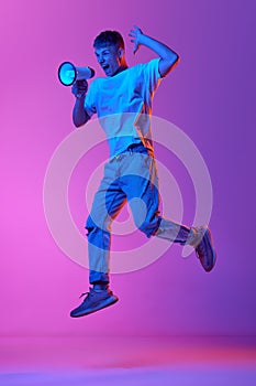 Emotional young man shouting in megaphone against gradient pink purple background in neon light. News