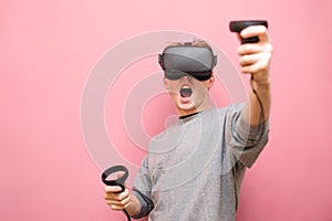 Emotional young man wearing a VR helmet on his head and casual wear playing virtual reality games with controllers in his hands,
