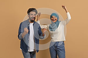 Emotional young muslim couple celebrating success, clenching fists and screaming