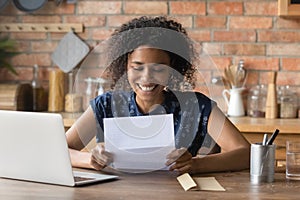 Emotional young positive african ethnicity woman reading paper correspondence.