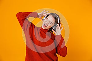 Emotional young pretty woman posing isolated over yellow wall background listening music with headphones