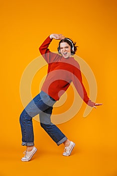 Emotional young pretty woman posing isolated over yellow wall background listening music with headphones