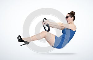 Emotional young woman in blue dress and sunglasses with a car steering wheel. Lady driver concept