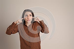 Emotional young woman covering ears with fingers on beige background, space for text