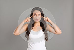 Emotional young woman covering ears with fingers on grey background