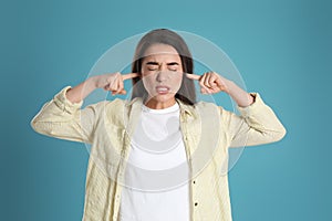 Emotional young woman covering ears with fingers on light blue background