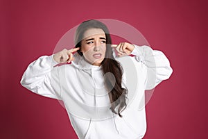 Emotional young woman covering ears with fingers on pink background