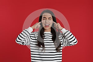 Emotional young woman covering ears with fingers on red background