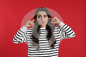 Emotional young woman covering ears with fingers on red background