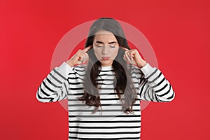 Emotional young woman covering ears with fingers on red background