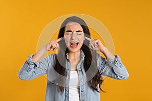 Emotional young woman covering ears with fingers on yellow