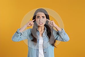 Emotional young woman covering ears with fingers on yellow background