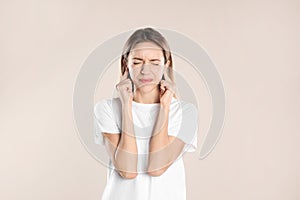 Emotional young woman covering her ears with fingers on beige background