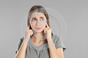 Emotional young woman covering her ears with fingers on grey background