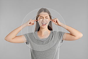 Emotional young woman covering her ears with fingers on grey background