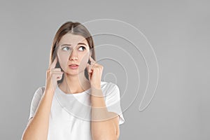 Emotional young woman covering her ears with fingers on grey background. Space for text