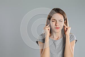 Emotional young woman covering her ears with fingers on grey background. Space for text