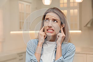 Emotional young woman covering her ears with fingers at home