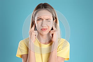 Emotional young woman covering her ears with fingers on light blue background