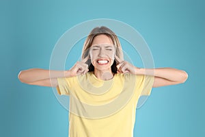 Emotional young woman covering her ears with fingers on light blue background