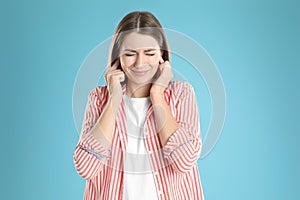 Emotional young woman covering her ears with fingers on light blue background