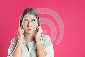 Emotional young woman covering her ears with fingers on pink background. Space for text