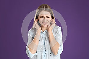 Emotional young woman covering her ears with fingers on purple background