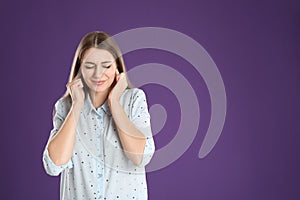 Emotional young woman covering her ears with fingers on purple background. Space for text