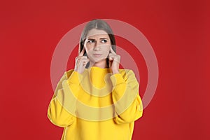 Emotional young woman covering her ears with fingers on red background