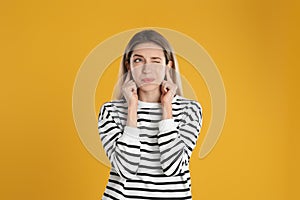 Emotional young woman covering her ears with fingers on yellow background