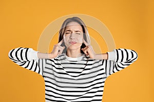 Emotional young woman covering her ears with fingers on yellow background