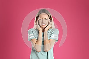 Emotional young woman covering her ears on pink background