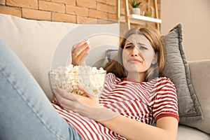 Emotional young woman eating popcorn while watching TV at home