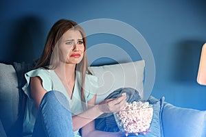 Emotional young woman eating popcorn while watching TV at home