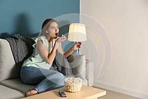 Emotional young woman eating popcorn while watching TV at home