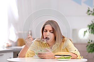 Emotional young woman eating salad instead of sandwich