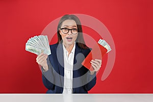 Emotional young woman with money and wallet at table on background