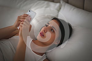 Emotional young woman with nomophobia using smartphone in bed at night. Insomnia concept